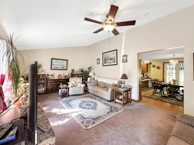 living room featuring ceiling fan with notable chandelier, carpet flooring, and vaulted ceiling