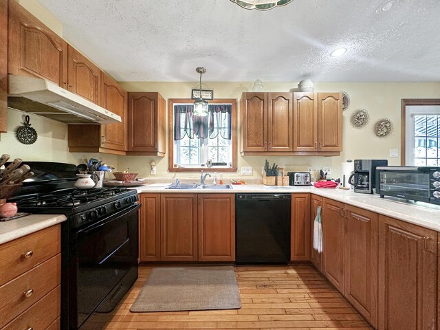 kitchen featuring a textured ceiling, sink, light hardwood / wood-style flooring, black appliances, and decorative light fixtures