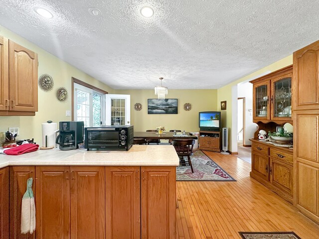 kitchen with kitchen peninsula, light hardwood / wood-style floors, hanging light fixtures, and a textured ceiling