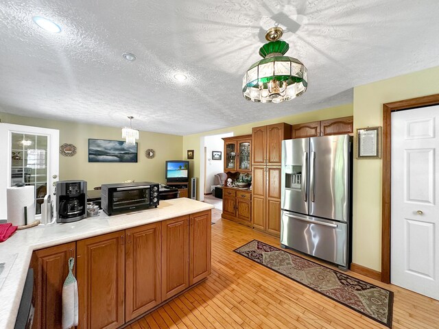 kitchen with a textured ceiling, light hardwood / wood-style floors, pendant lighting, and stainless steel fridge with ice dispenser