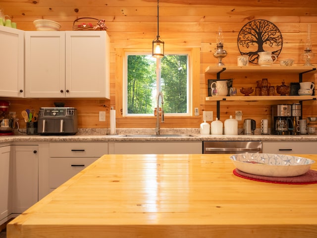 kitchen featuring sink, wood counters, hanging light fixtures, white cabinets, and stainless steel dishwasher