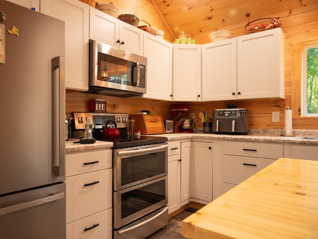 kitchen with lofted ceiling, wooden walls, wooden ceiling, white cabinetry, and appliances with stainless steel finishes