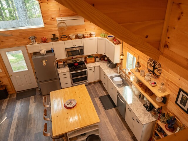 kitchen with stainless steel appliances, wood walls, dark hardwood / wood-style floors, and white cabinetry