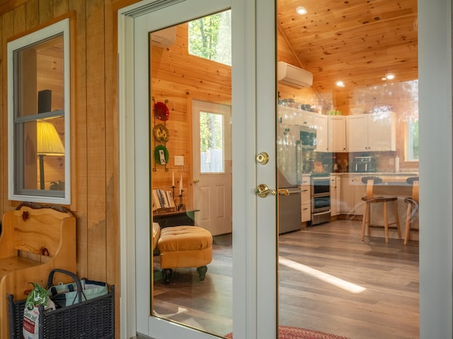 doorway to outside featuring light hardwood / wood-style floors, a wall mounted air conditioner, plenty of natural light, and vaulted ceiling