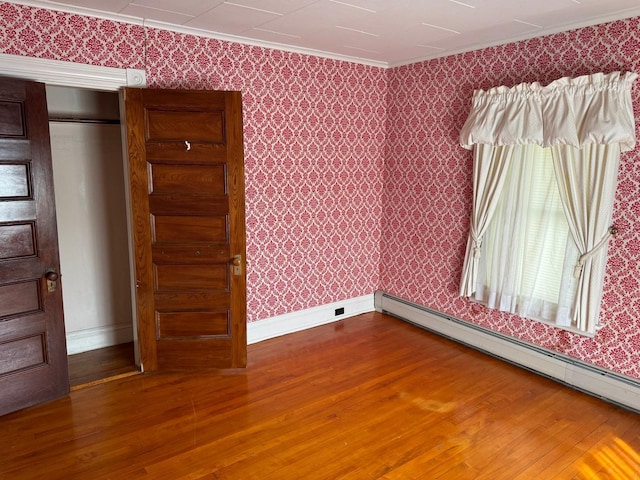 unfurnished bedroom featuring ornamental molding, a baseboard radiator, a closet, and hardwood / wood-style floors