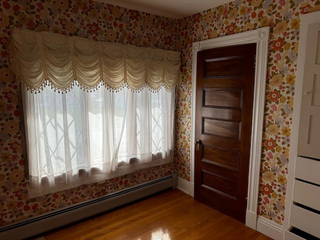 empty room with baseboard heating, hardwood / wood-style floors, and a healthy amount of sunlight