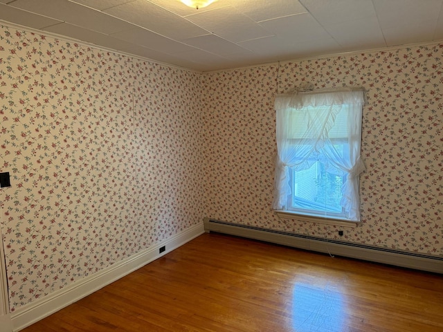 spare room with crown molding, baseboard heating, and hardwood / wood-style flooring