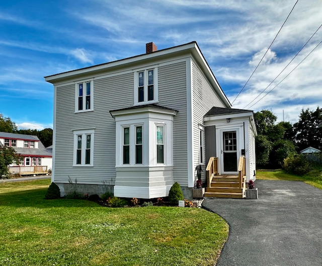 view of front of property with a front lawn, aphalt driveway, and a chimney