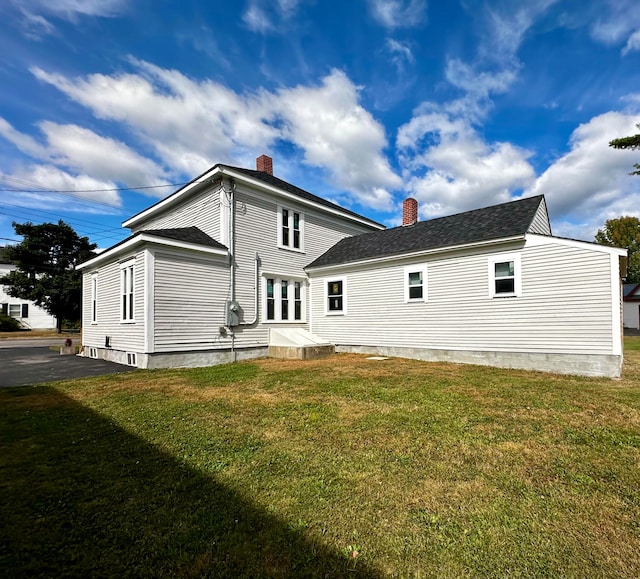 rear view of property featuring a yard, driveway, roof with shingles, and a chimney