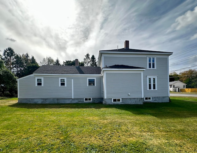 back of property with a shingled roof, a yard, and a chimney