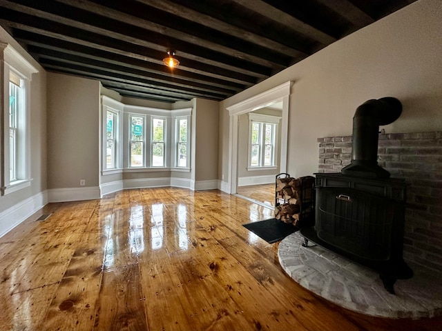 living area featuring beam ceiling, a wood stove, baseboards, and wood-type flooring