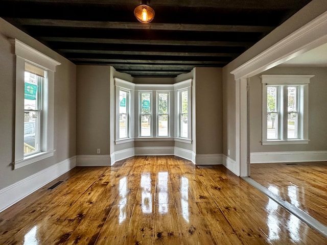 spare room with visible vents, wood-type flooring, baseboards, and beam ceiling