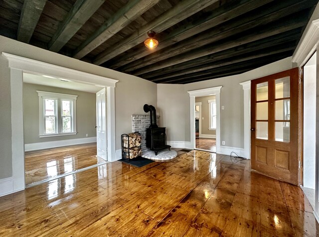 unfurnished living room featuring beam ceiling, a wood stove, wood finished floors, and baseboards