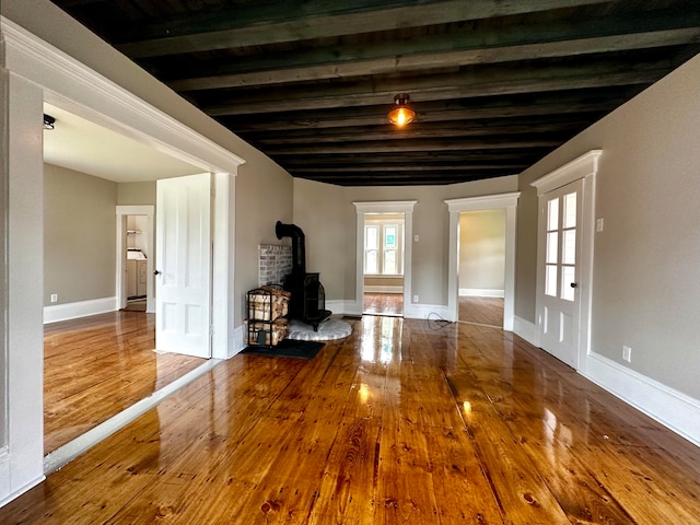 empty room featuring wood ceiling, a wood stove, beamed ceiling, and hardwood / wood-style floors