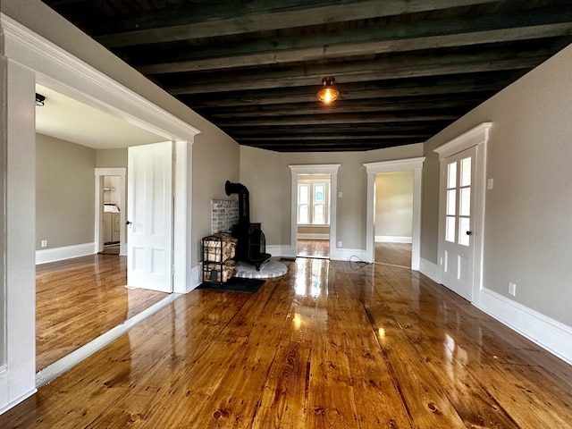 112 S St, Calais, ME 04619 - unfurnished living room featuring a wood stove, hardwood / wood-style flooring, beam ceiling, and baseboards