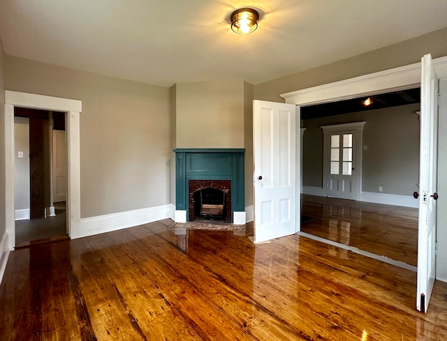 unfurnished living room featuring a fireplace with flush hearth, baseboards, and wood-type flooring