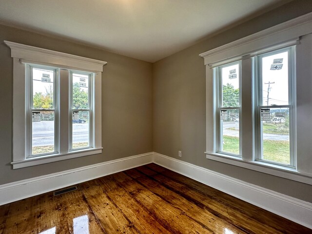 spare room featuring visible vents, baseboards, plenty of natural light, and dark wood finished floors