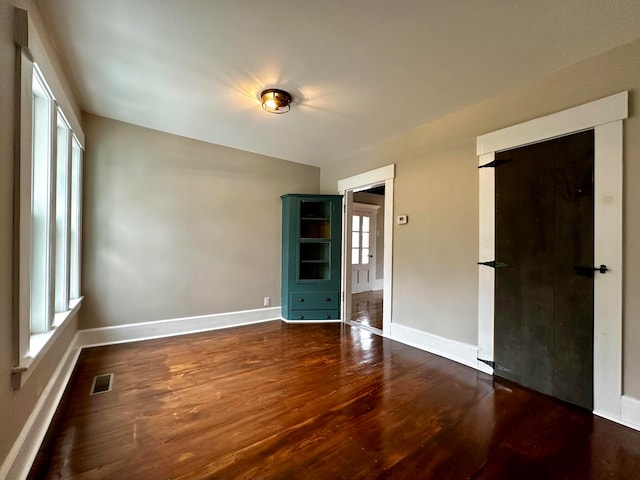 spare room with dark wood-style floors, visible vents, and baseboards