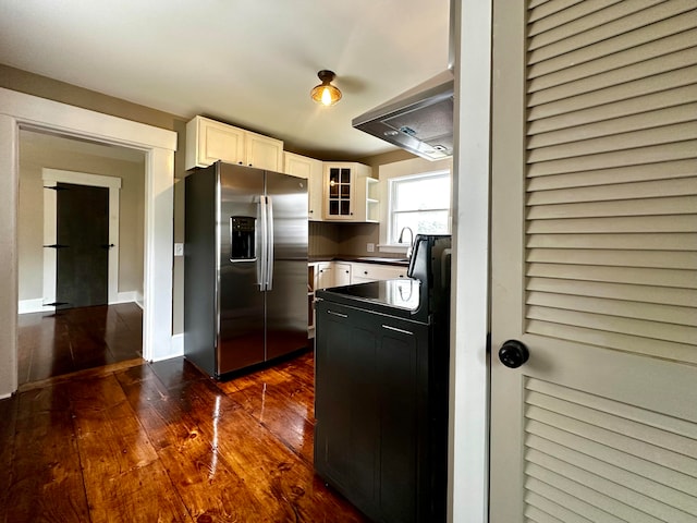 kitchen with dark wood-type flooring, dark countertops, white cabinetry, stainless steel fridge with ice dispenser, and glass insert cabinets