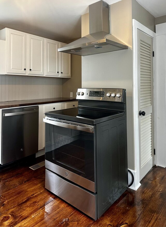 kitchen with wall chimney exhaust hood, white cabinets, appliances with stainless steel finishes, and dark wood-type flooring