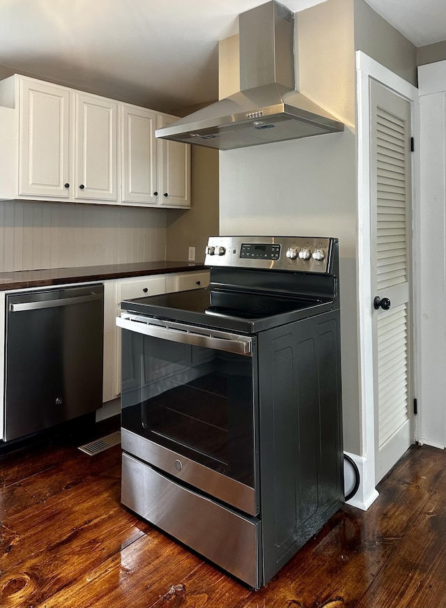112 S St, Calais, ME 04619 - kitchen featuring appliances with stainless steel finishes, wall chimney range hood, dark wood-style flooring, white cabinets, and dark countertops