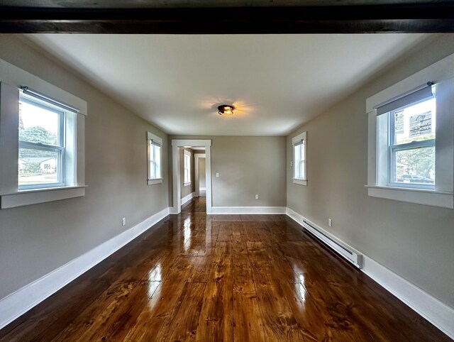 empty room featuring beamed ceiling, plenty of natural light, dark wood-type flooring, and a baseboard heating unit