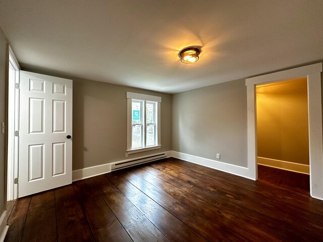 empty room with baseboard heating and dark hardwood / wood-style flooring