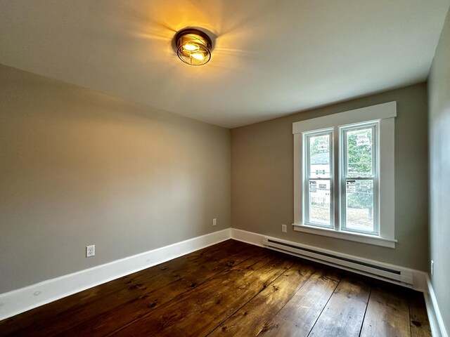 unfurnished room with a baseboard heating unit, baseboards, and dark wood-style floors