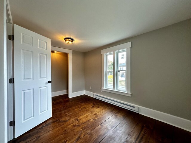 empty room featuring dark wood-type flooring and a baseboard heating unit