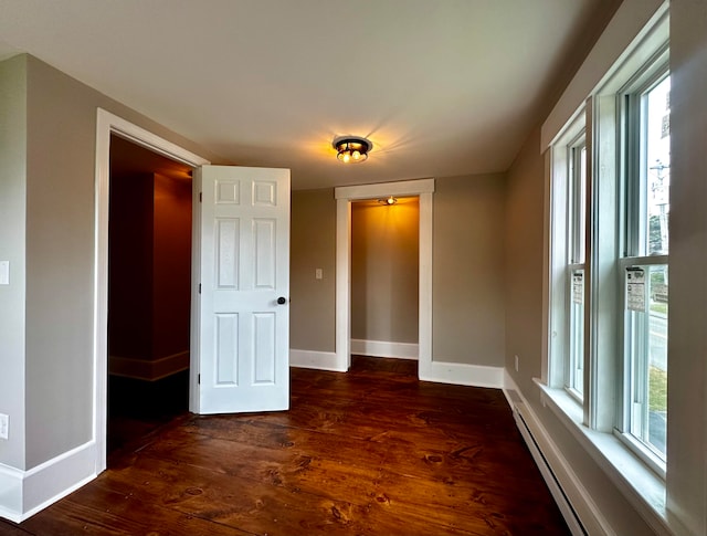 unfurnished bedroom featuring a baseboard heating unit and dark wood-type flooring