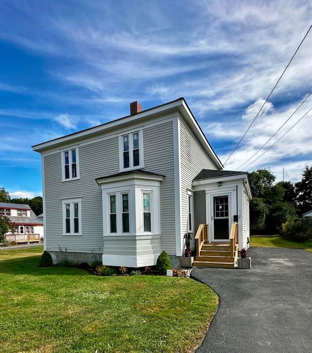 view of front of property featuring entry steps, a front yard, driveway, and a chimney