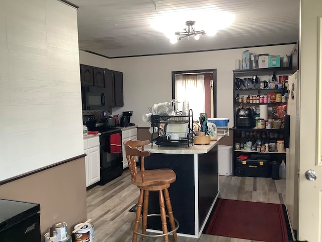 kitchen with white cabinets, a kitchen island, black appliances, a breakfast bar area, and light wood-type flooring