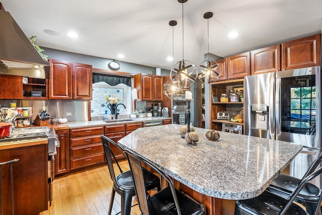 kitchen featuring light hardwood / wood-style floors, wall chimney exhaust hood, pendant lighting, a kitchen bar, and a center island