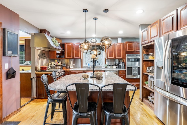 kitchen with appliances with stainless steel finishes, backsplash, light wood-type flooring, a center island, and extractor fan