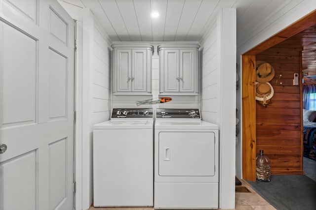 laundry area featuring washing machine and dryer, wooden walls, light tile patterned flooring, and cabinets