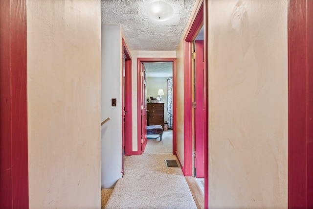 hallway featuring light carpet and a textured ceiling