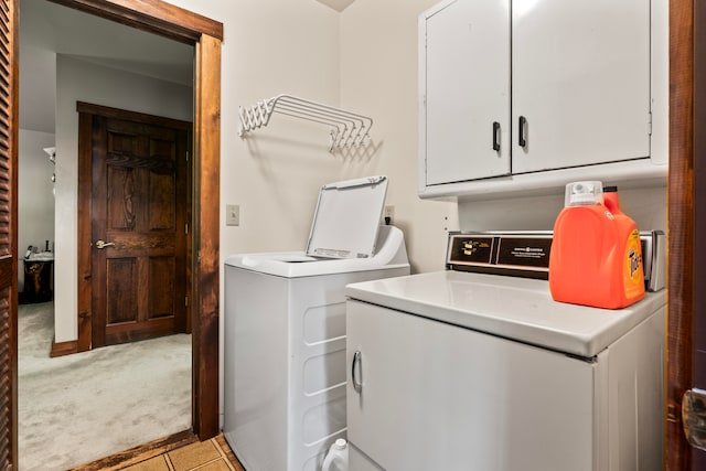 clothes washing area featuring light carpet, washing machine and clothes dryer, and cabinets