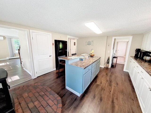 kitchen featuring white cabinets, a kitchen island, dark hardwood / wood-style floors, and black refrigerator