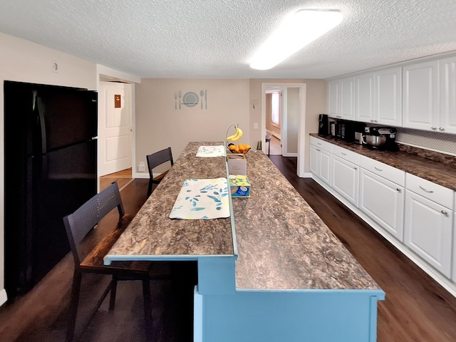 interior space with white cabinets, a breakfast bar area, black fridge, and dark hardwood / wood-style flooring