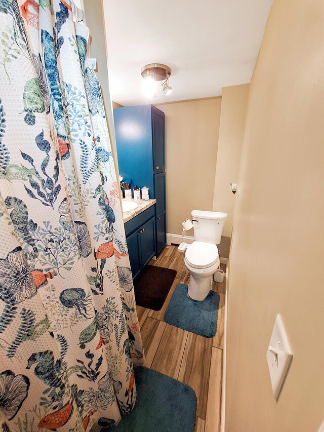 bathroom with vanity, toilet, baseboard heating, a shower with curtain, and hardwood / wood-style floors