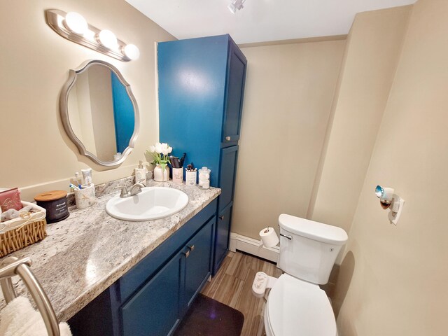 bathroom with a baseboard heating unit, hardwood / wood-style flooring, vanity, and toilet