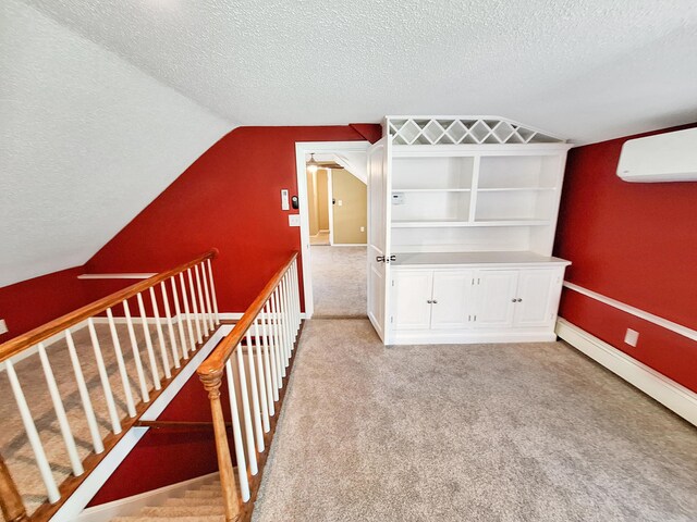 stairway with lofted ceiling, a textured ceiling, a baseboard heating unit, carpet, and a wall unit AC