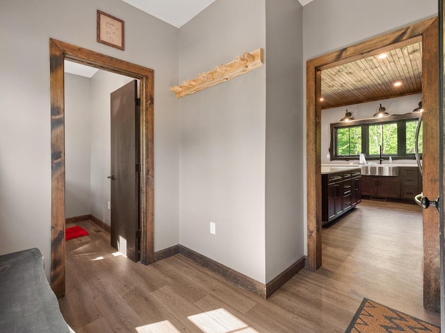 hallway with light hardwood / wood-style flooring, wooden ceiling, and sink