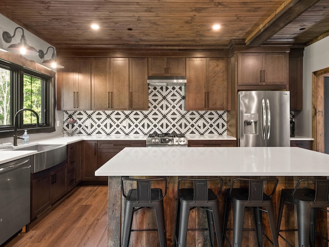 kitchen with appliances with stainless steel finishes, dark hardwood / wood-style floors, a kitchen bar, and a center island