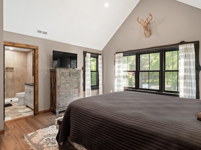 bedroom with light hardwood / wood-style floors, ensuite bathroom, and high vaulted ceiling