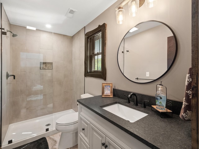 bathroom featuring a tile shower, vanity, and toilet