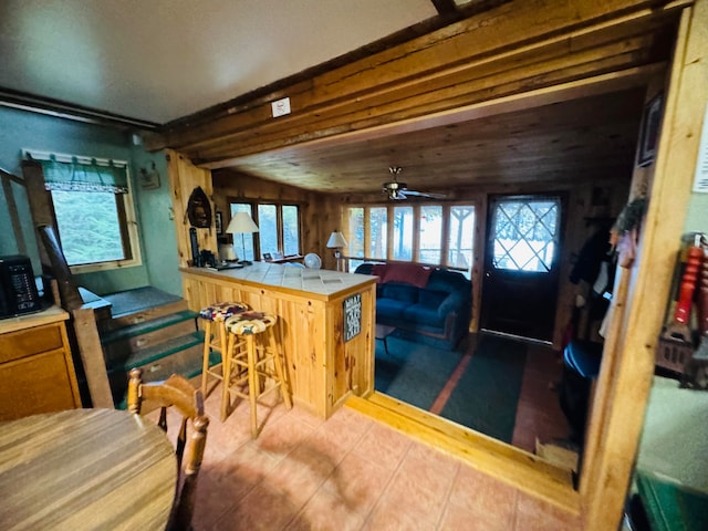 kitchen with ceiling fan, lofted ceiling, kitchen peninsula, tile countertops, and a breakfast bar