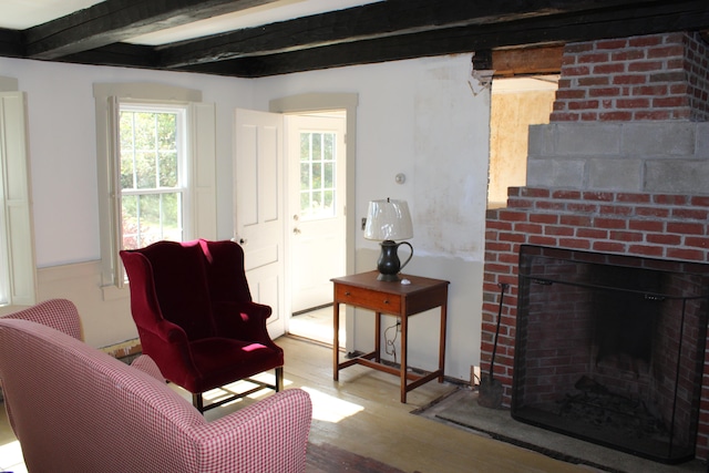 living room with a brick fireplace, beamed ceiling, and light wood-type flooring