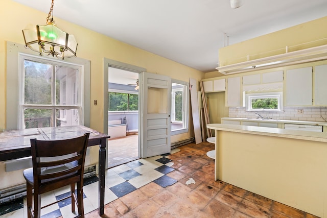 kitchen with a wealth of natural light, white cabinetry, hanging light fixtures, and backsplash