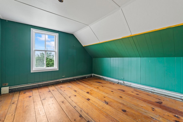 additional living space with a baseboard radiator, lofted ceiling, wood walls, and hardwood / wood-style flooring